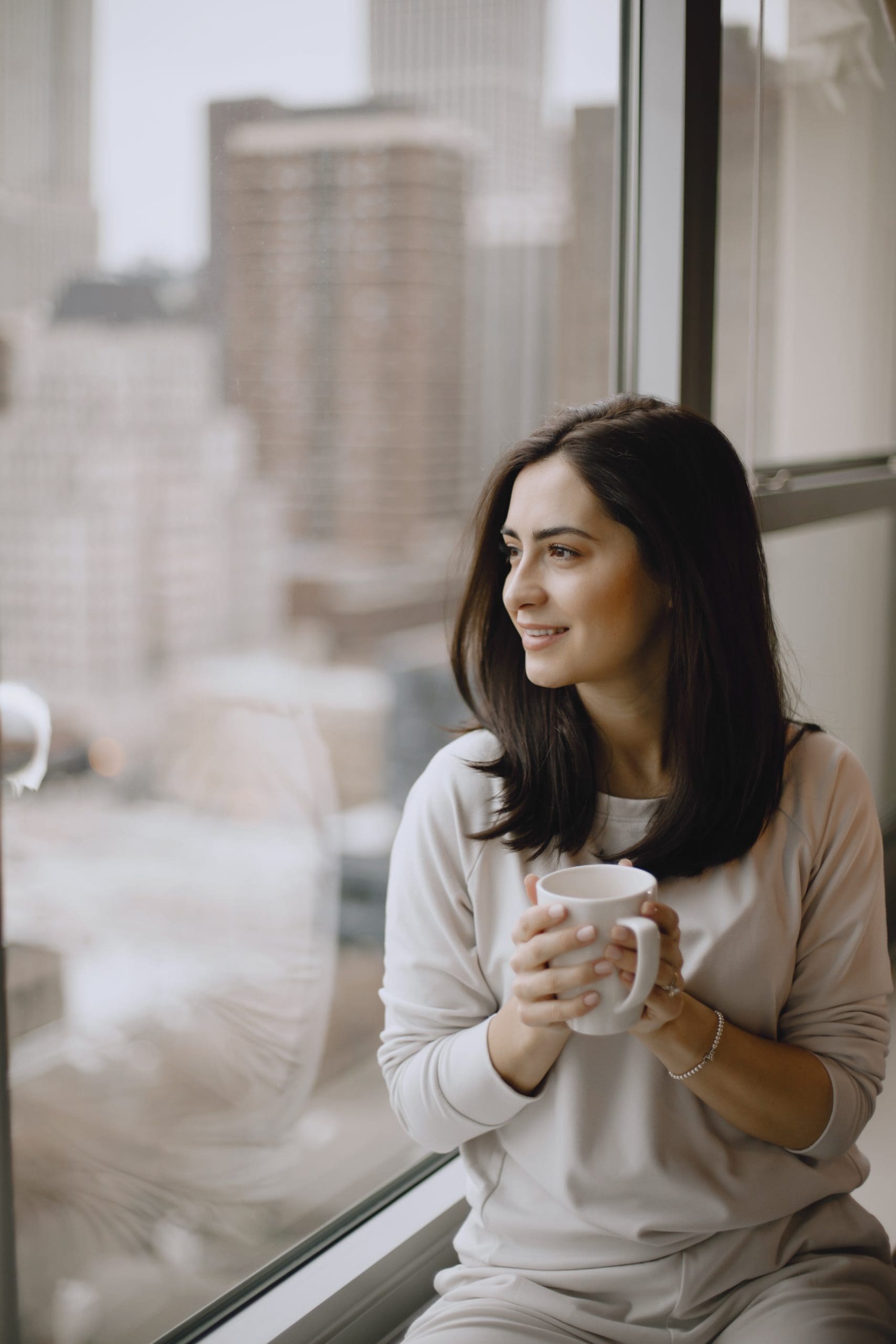 Brunette sitting on a windowsill and drinks a coffee