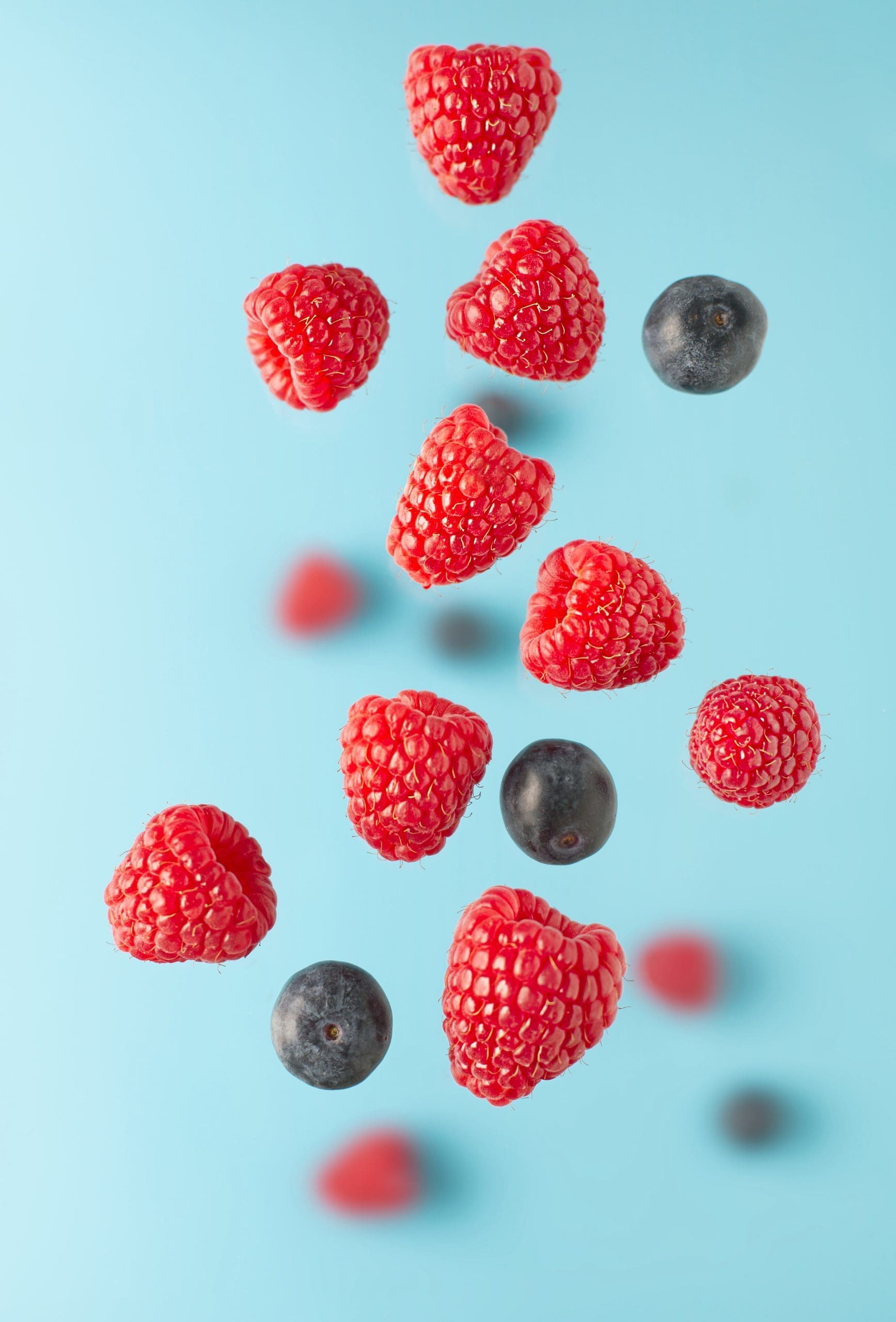 Flying berries over blue table. Falling berries such as raspberry fruits and blueberries